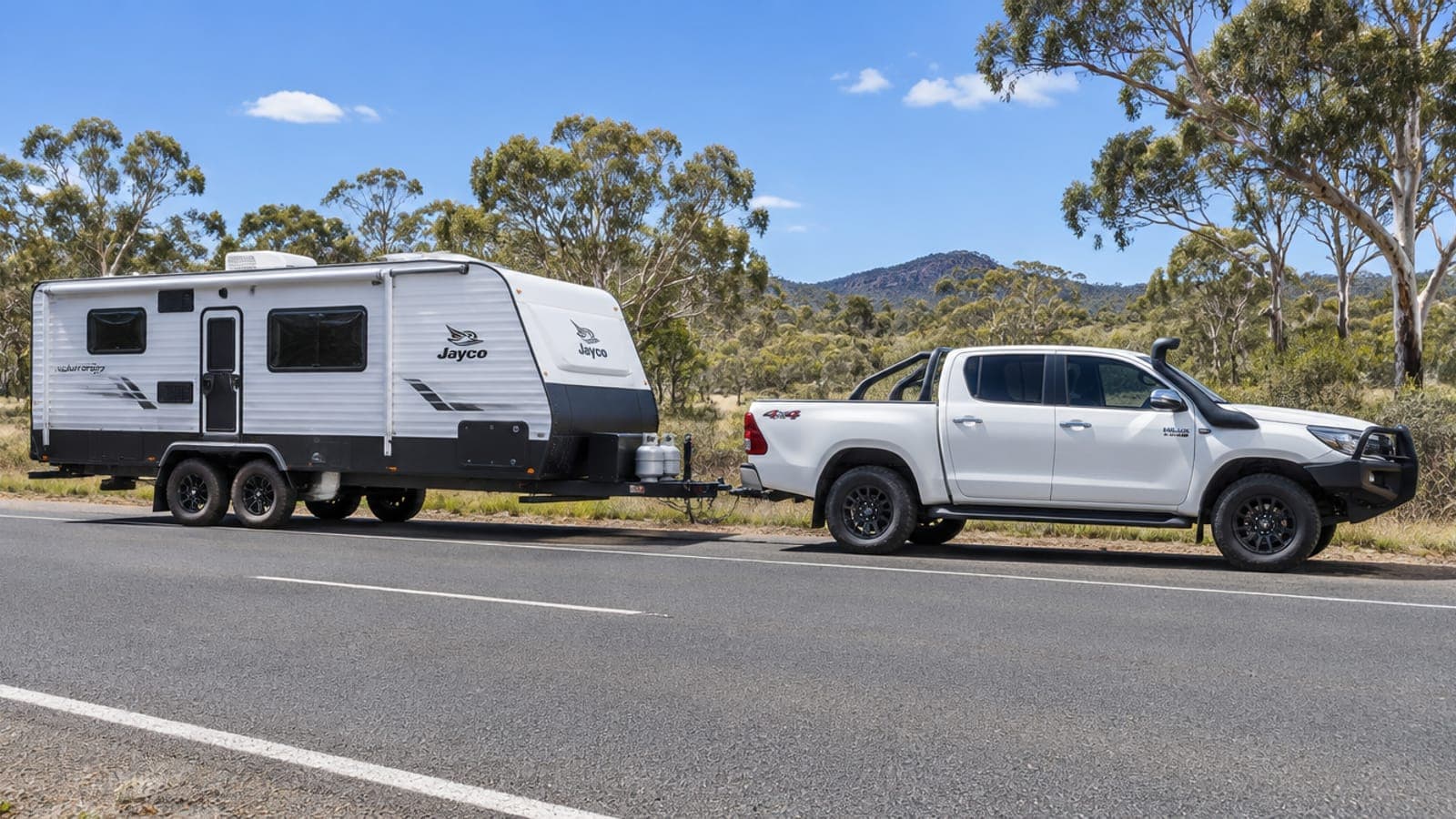 A dual-cab ute towing a touring caravan on a regional road